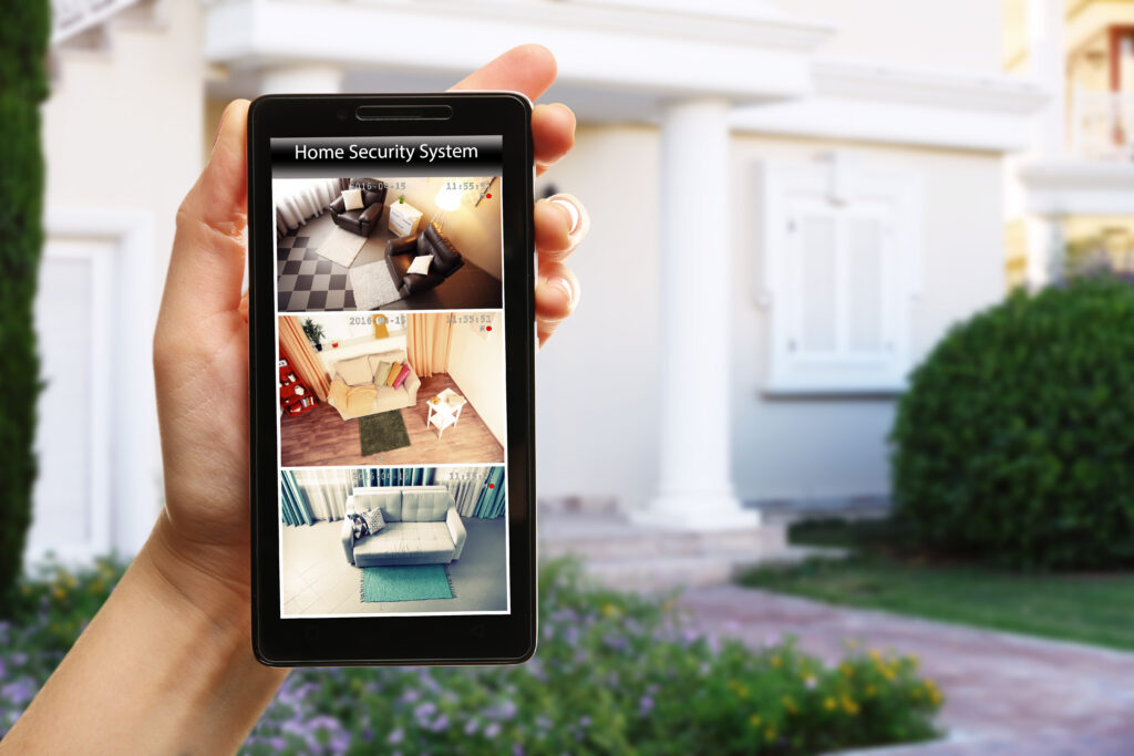 Female hand holding a smartphone on blurred house background. Home security system concept
